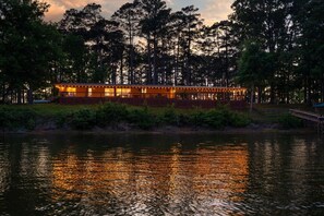 A lakeside lodge with a dining area overlooking the water, surrounded by trees.
