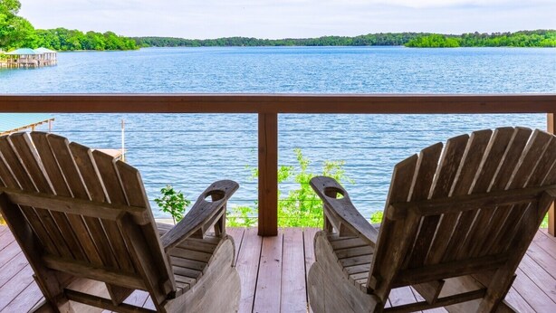 Una terraza de madera con dos sillas Adirondack mirando un lago.
