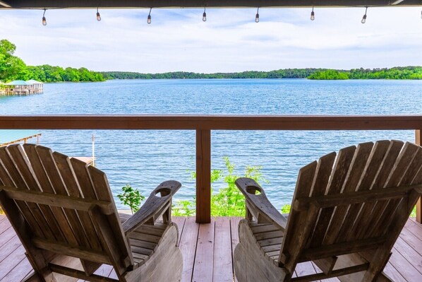 A wooden deck with two Adirondack chairs facing a lake.