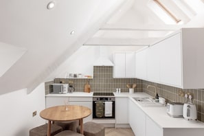 Una cocina moderna con armarios blancos, horno integrado, microondas y cafetera.
