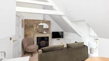 Ein modernes Schlafzimmer im Loft-Stil mit schrägem Dach, Kamin aus Naturstein, Flachbildfernseher und einer gemütlichen Sitzecke.