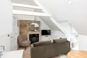 Un dormitorio tipo loft moderno con techo inclinado, chimenea de piedra, televisor de pantalla plana y una zona de estar acogedora.