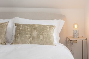 A bed with white bedding and two textured pillows, a bedside table with a lamp, and a wall switch. - Stylish Apartment in Converted 18th-Century Guest House | Central Rothbury (Rothbury)