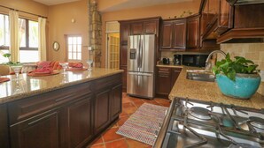 A kitchen with dark wooden cabinets, a stainless steel refrigerator, a gas stove, and a blue bowl with green plants.