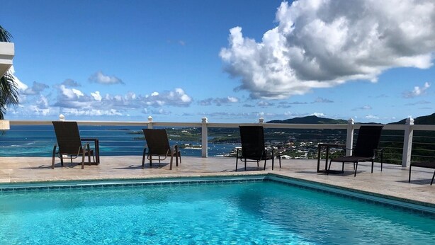 A clear blue pool with lounge chairs and a view of the ocean.