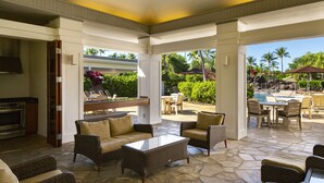A covered outdoor area with wicker furniture, a dining table, and a pool view.