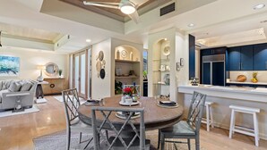 A spacious living area with a round dining table, grey chairs, and a ceiling fan.