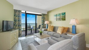 Un salon comprenant un canapé, deux fauteuils, une table basse, un téléviseur et un balcon avec vue.