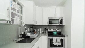 A modern kitchen with white cabinets, a stainless steel microwave, a stove, and a sink. - Bike to Beach-Spacious With Patio BBQ Plus Game Room (Hallandale Beach)