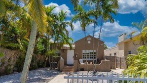 A house with a paved driveway, a white picket fence, and palm trees. - Bike to Beach-Spacious With Patio BBQ Plus Game Room (Hallandale Beach)