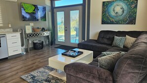 A modern living room with a dark brown sofa, a white coffee table, and a large painting on the wall. - Modern container cabin on 13 acre country estate (Sequim)