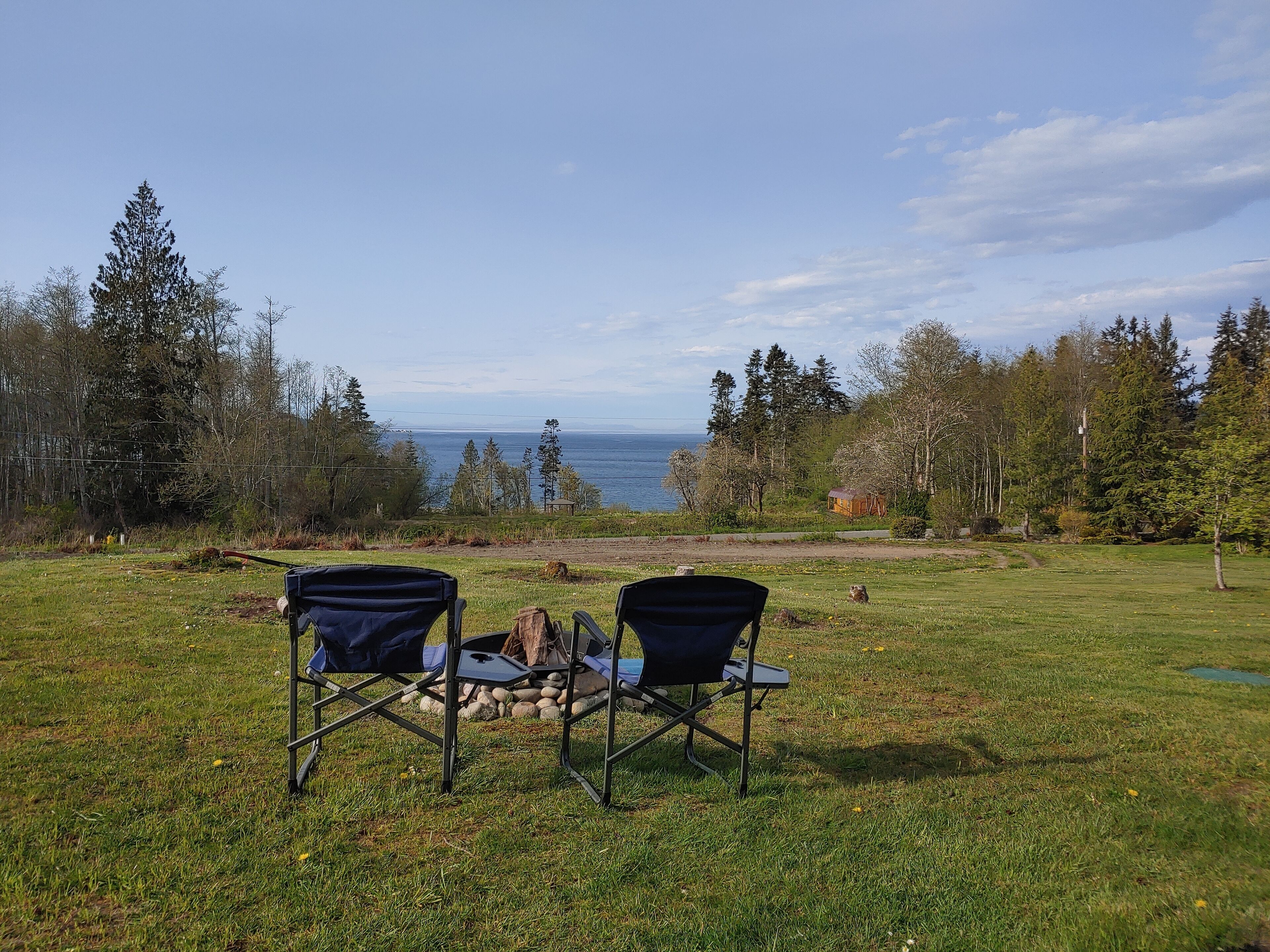 A grassy area with two folding chairs facing a body of water, surrounded by trees and a small structure.