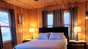 Un dormitorio acogedor con techo de madera, una cama con colcha blanca, dos mesitas de noche con lámparas y un ventilador de techo.