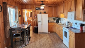 Una cocina tipo cabaña de madera con comedor, armarios de madera, refrigerador, estufa, microondas y ventilador de techo.