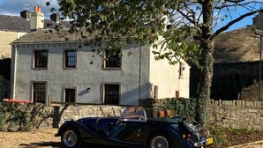 Un cotxe convertible negre antic estacionat davant d'un edifici de pedra amb diverses finestres i una xemeneu.