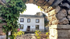 Un arc de pedra emmarca un edifici blanc amb nombroses finestres i una porta, envoltat de vegetació.