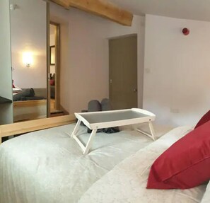 A bedroom with a bed, a small table, a door, and a mirror.