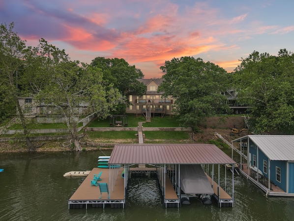 A lakeside property with a dock, a swing chair, and a house with a deck.