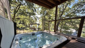 Een hottub op een houten terras, met uitzicht op bomen en een tuinhuisje op de achtergrond.
