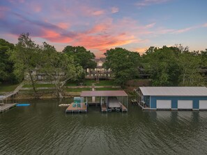 A lakeside property with a dock, a covered seating area, and a large house with a deck.