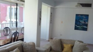 Un salón con dos sofás color beige, un cojín amarillo y un cuadro de delfines en la pared.