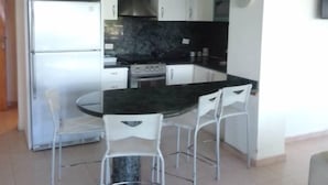 Una cocina compacta con una isla central, armarios blancos, horno empotrado y refrigerador de acero inoxidable.