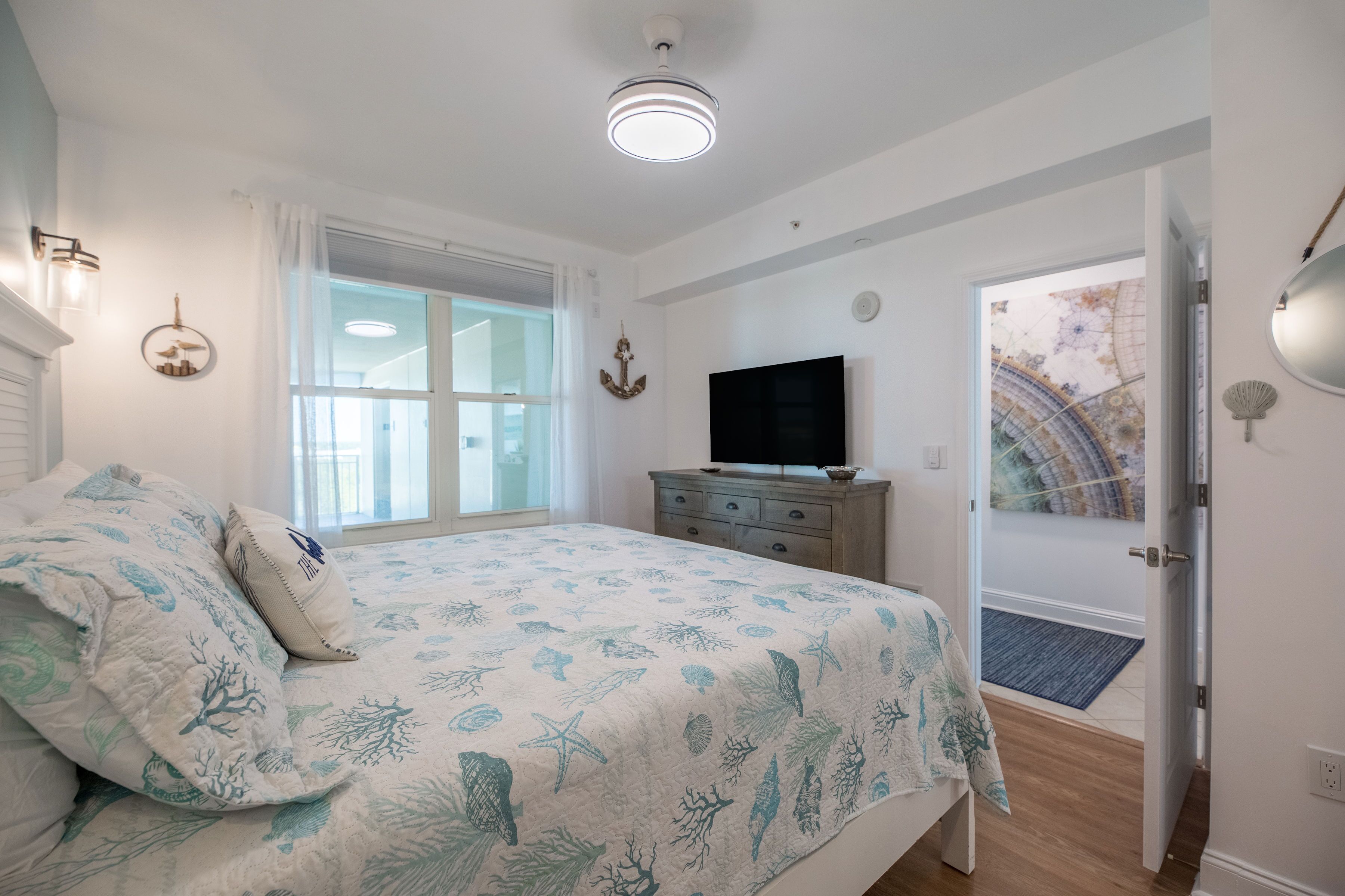 Une chambre à coucher comprenant un lit, une télévision, une commode, une fenêtre avec des rideaux et une porte donnant sur une autre pièce.