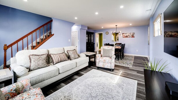 Uma sala de estar com sofá, poltronas, mesa de centro, tapete, escada e área de jantar com mesa e cadeiras.