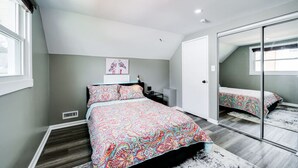 Quarto com cama, mesa de cabeceira, espelho e janela.