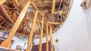 En trappe i træ med spiralformet design, med et rustikt interiør, synlige bjælker og en stenvæg.