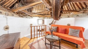 Et rustikt værelse med synlige træbjælker, et træbord, en orange sofa og et lille glastræ med en vase.