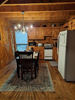 Una cocina rústica con armarios de madera, una mesa de comedor con sillas, un refrigerador y una estufa.
