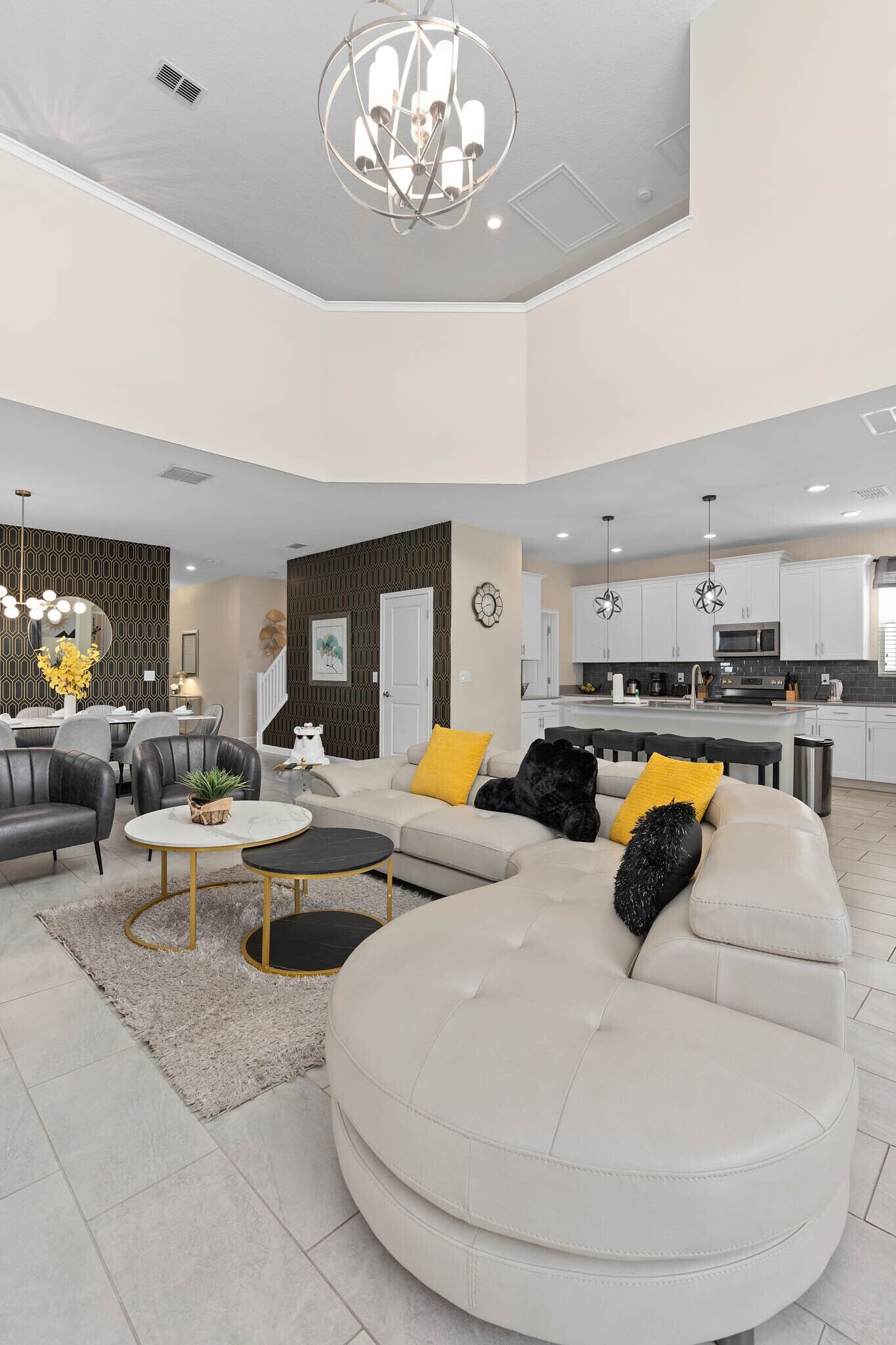 A spacious living area with a large L-shaped sofa, a round coffee table, and a dining area with a chandelier.