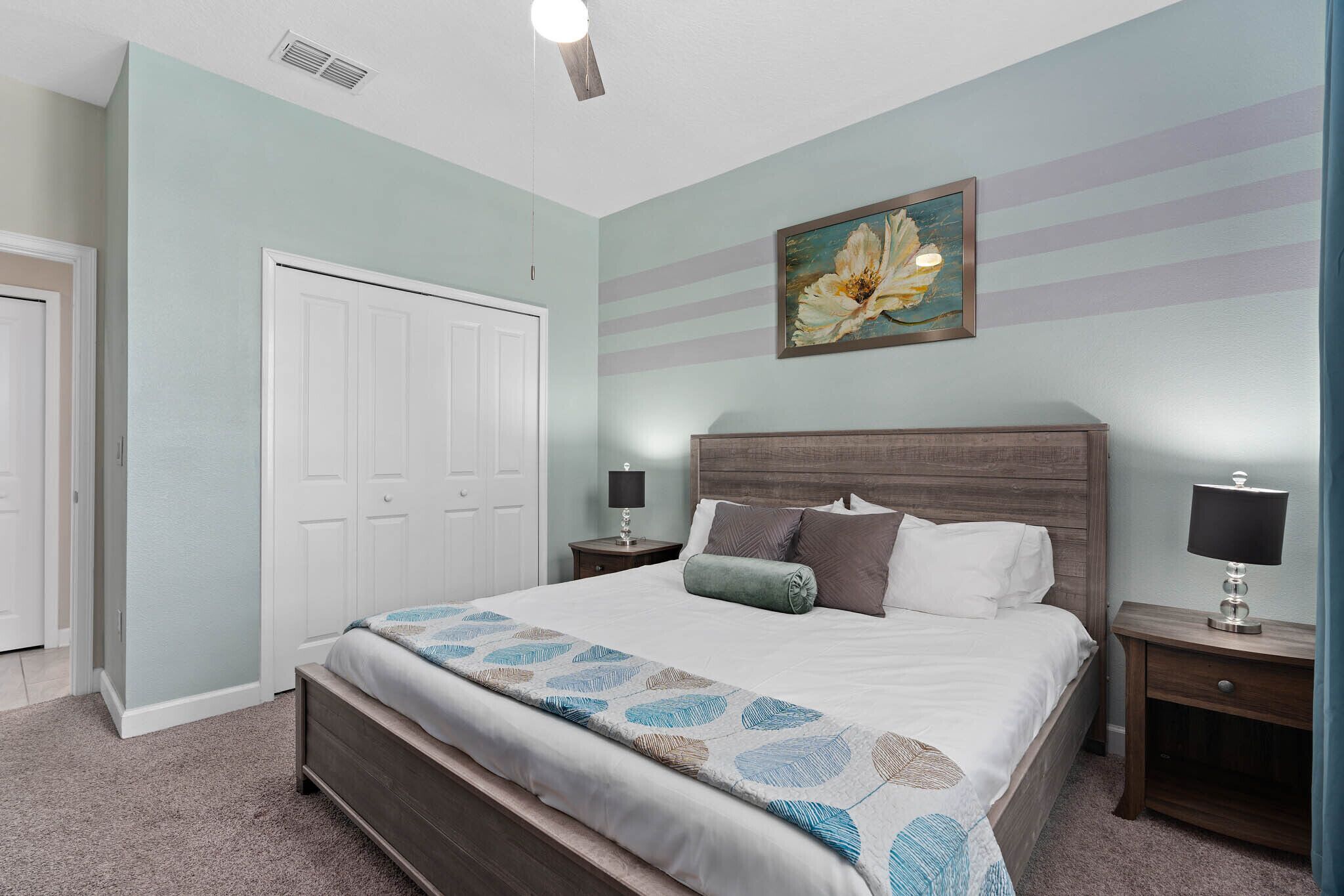 A bedroom with a bed, nightstands, a dresser, a door, and a painting on the wall.