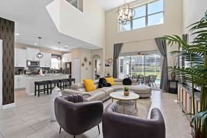 A spacious living area with a large sofa, a coffee table, and a dining area with a kitchen in the background.