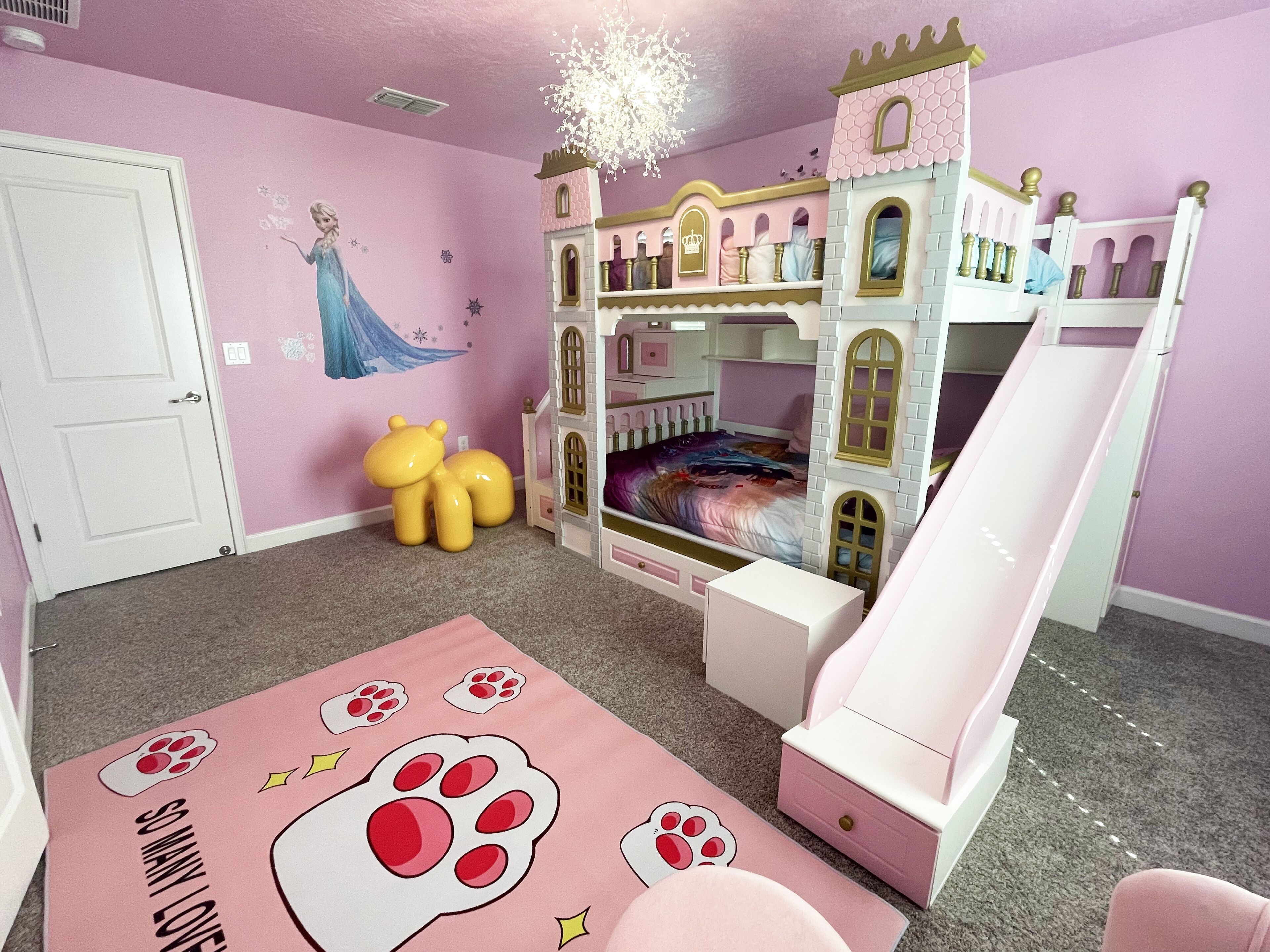 Un dormitorio infantil con una cama con forma de castillo, un tobogán y un mural en la pared.