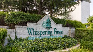 Schild für Whispering Pines Condominiums, umgeben von üppiger Vegetation.