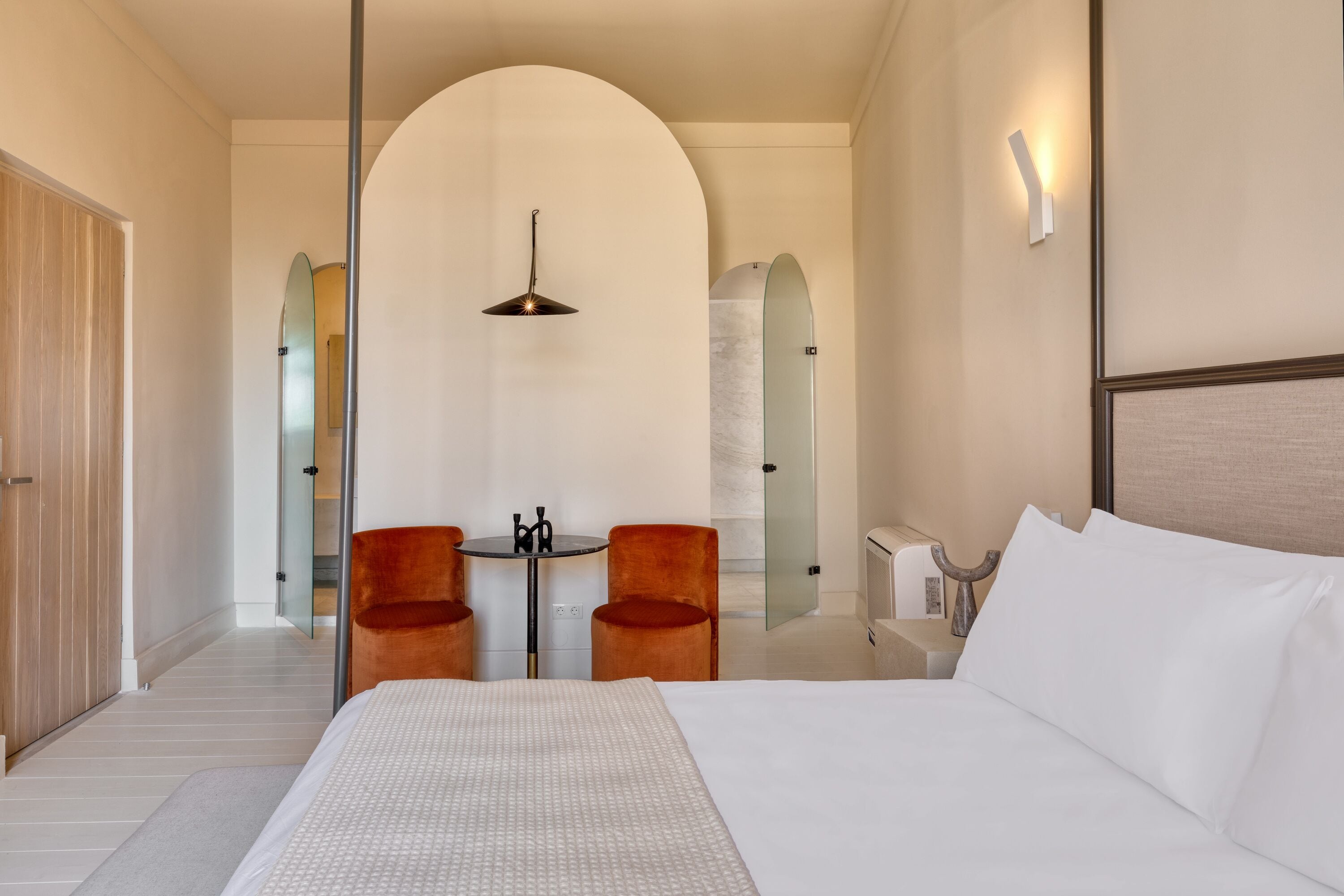 A modern hotel room with a large bed, two chairs, a small table, and a unique arched ceiling design.