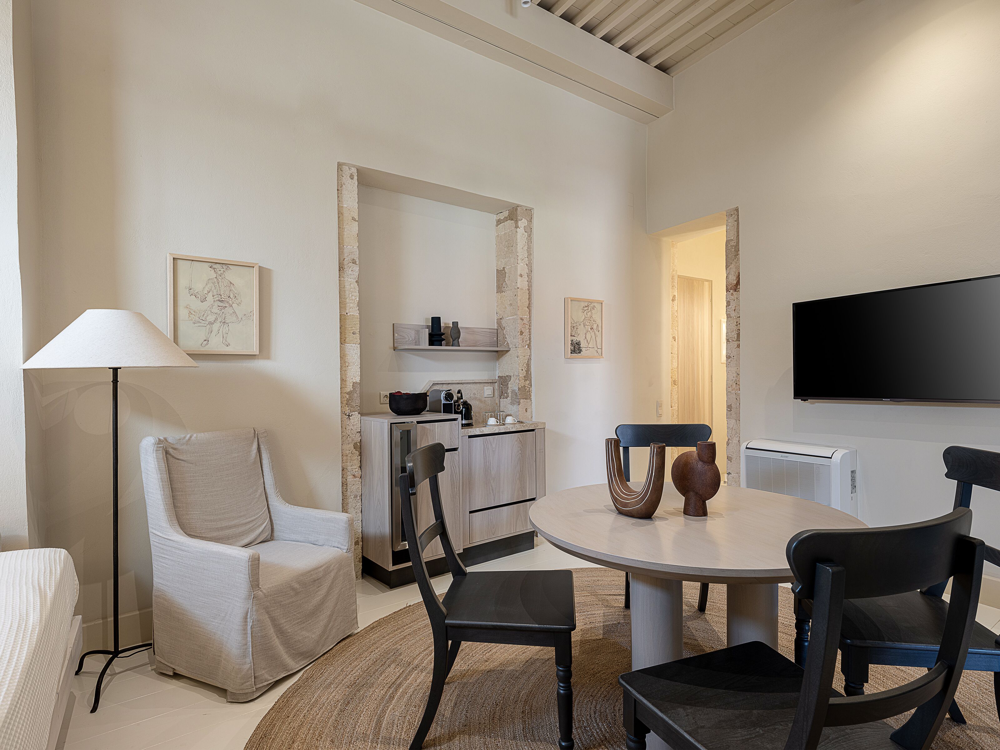 A modern living room with a round table, two chairs, a sofa, a floor lamp, and a flat-screen TV.
