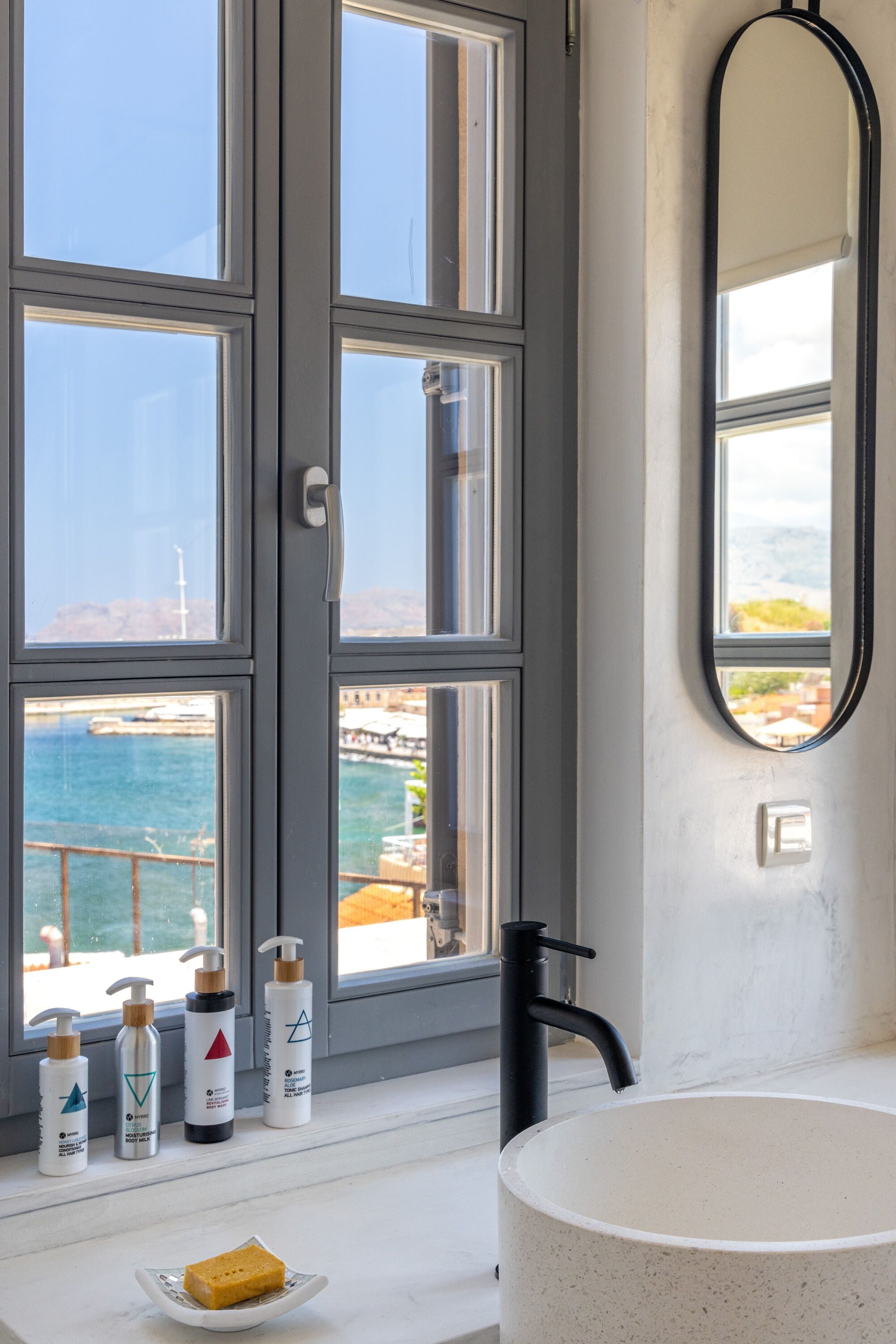 A bathroom with a large window, a bathtub, and toiletries on the windowsill.
