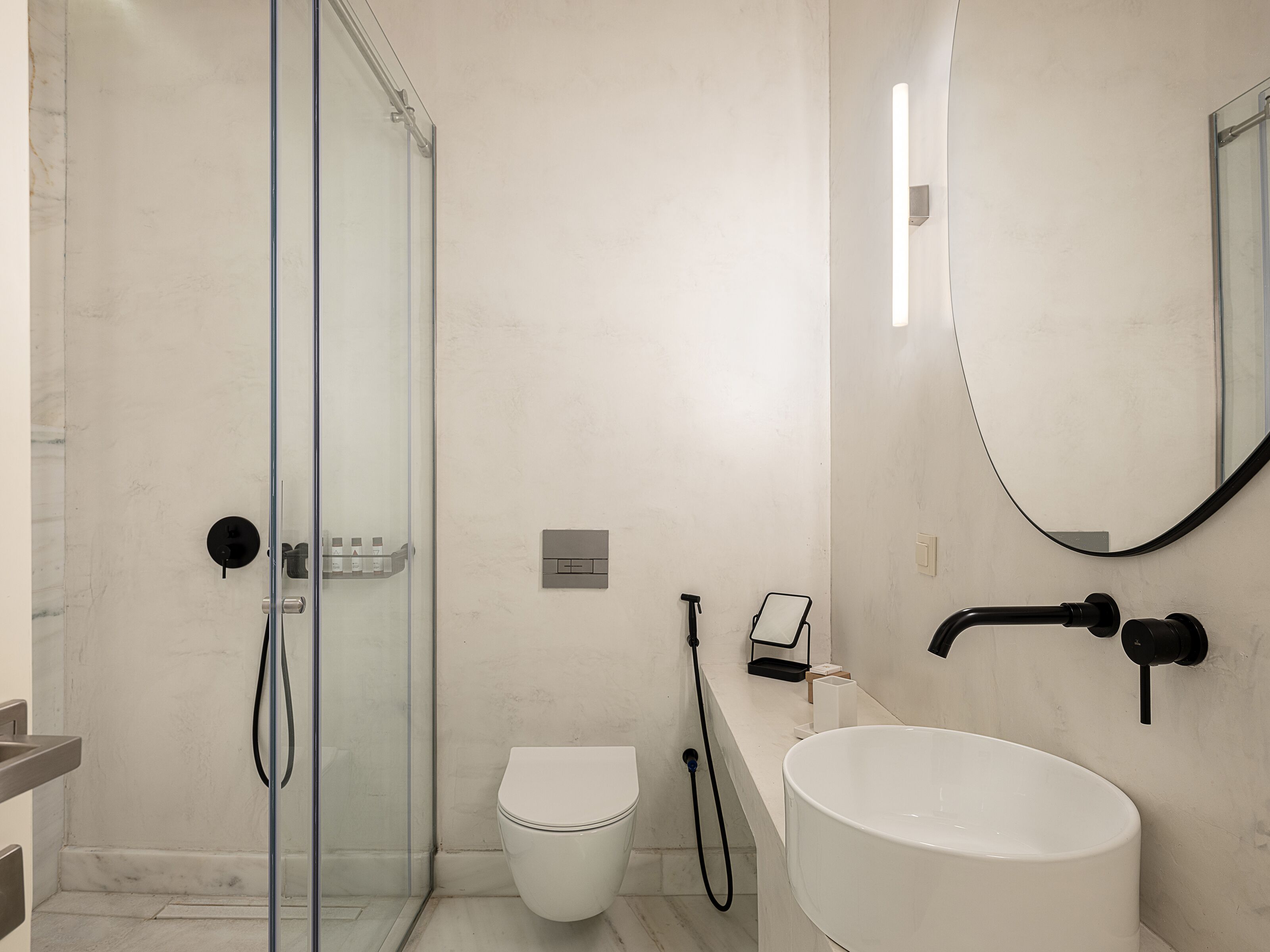 A modern bathroom with a glass shower enclosure, a white toilet, and a large sink with a mirror above it.