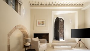 A modern bedroom with a large bed, a sofa, a small table, a fireplace, and a TV. - Azade Chania (Chania)