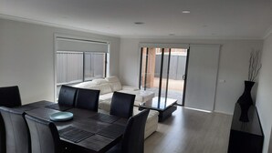 Een moderne eethoek met een donker houten tafel en zwarte stoelen, een witte bank en een glazen deur naar een terras.