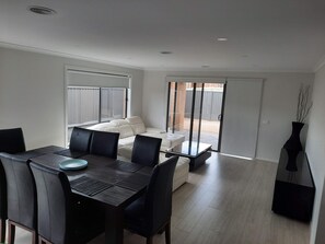 A modern dining area with a dark wooden table and black chairs, a white sofa, and a glass door leading to a patio. - The Jewel of Seachange | Modern Family Retreat Minutes from the Beach (Saint Leonards)