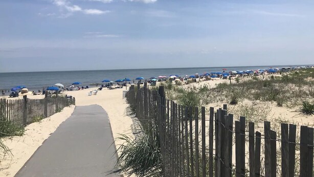 A beach with a wooden fence, a paved walkway, and beach umbrellas. - 4 Nights Left -Perfect Family-Friendly Condo 5 Houses from the Ocean-Beach Block (Dewey Beach)