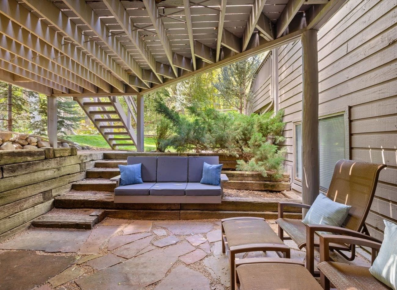 A covered outdoor seating area with a sofa and chairs, stone steps, and a wooden pergola.