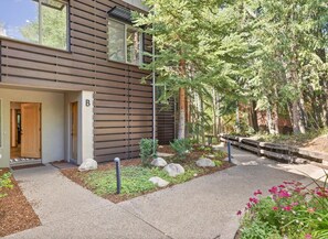 A modern building with a wooden facade, a visible entrance, and a landscaped garden with rocks and shrubs.