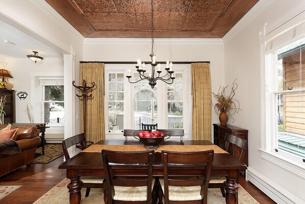 Un comedor con una mesa de madera, sillas, una araña y vistas amplias a través de grandes ventanas.