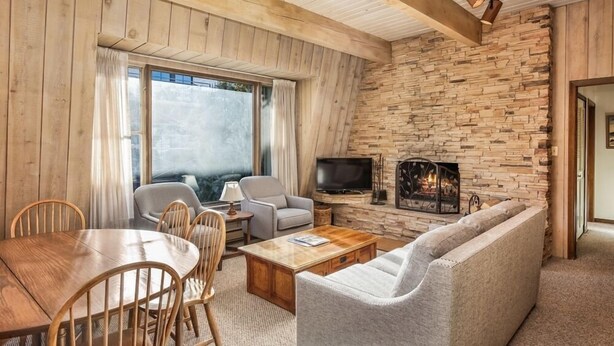 Una sala de estar acogedora con pared de piedra, vigas de madera en el techo, chimenea y televisor.