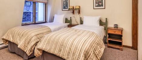 A bedroom with two beds, a window with a view, and a nightstand with a lamp.
